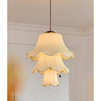 Lit three-tier pleated pendant from Clérachic hanging below a ceiling with white cornice moulding, its scalloped edges glowing warm.
