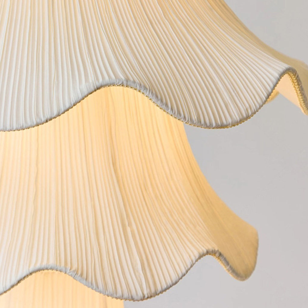 Close view of the fine vertical pleats and wavy trimmed edge of the fabric shade on this Clérachic pendant, lit from within.