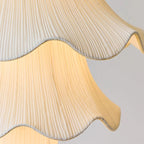 Close view of the fine vertical pleats and wavy trimmed edge of the fabric shade on this Clérachic pendant, lit from within.