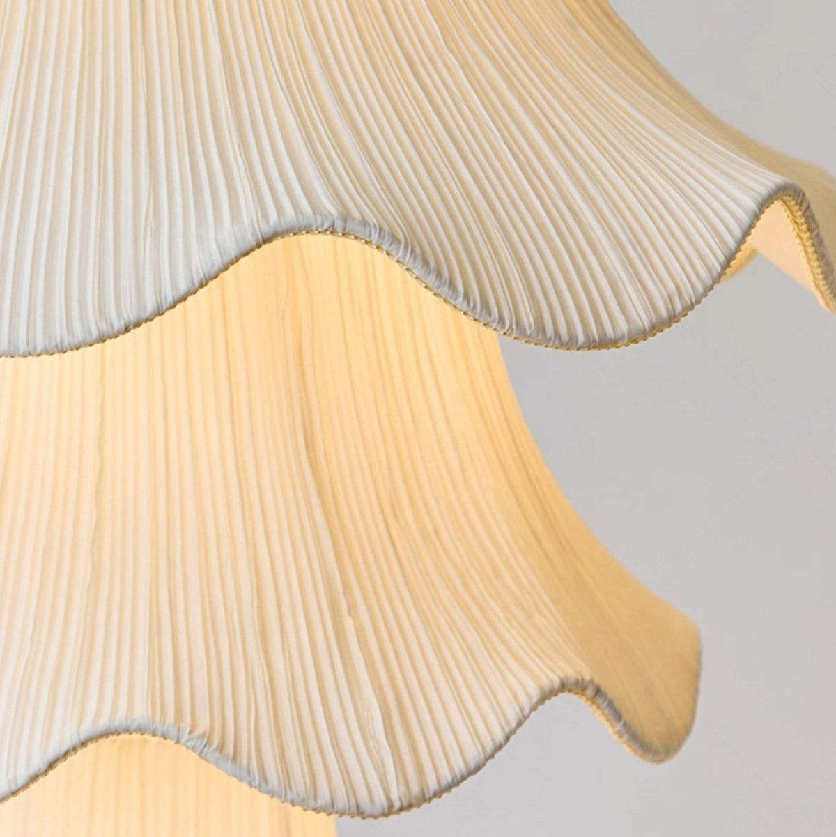 Close view of the fine vertical pleats and wavy trimmed edge of the fabric shade on this Clérachic pendant, lit from within.