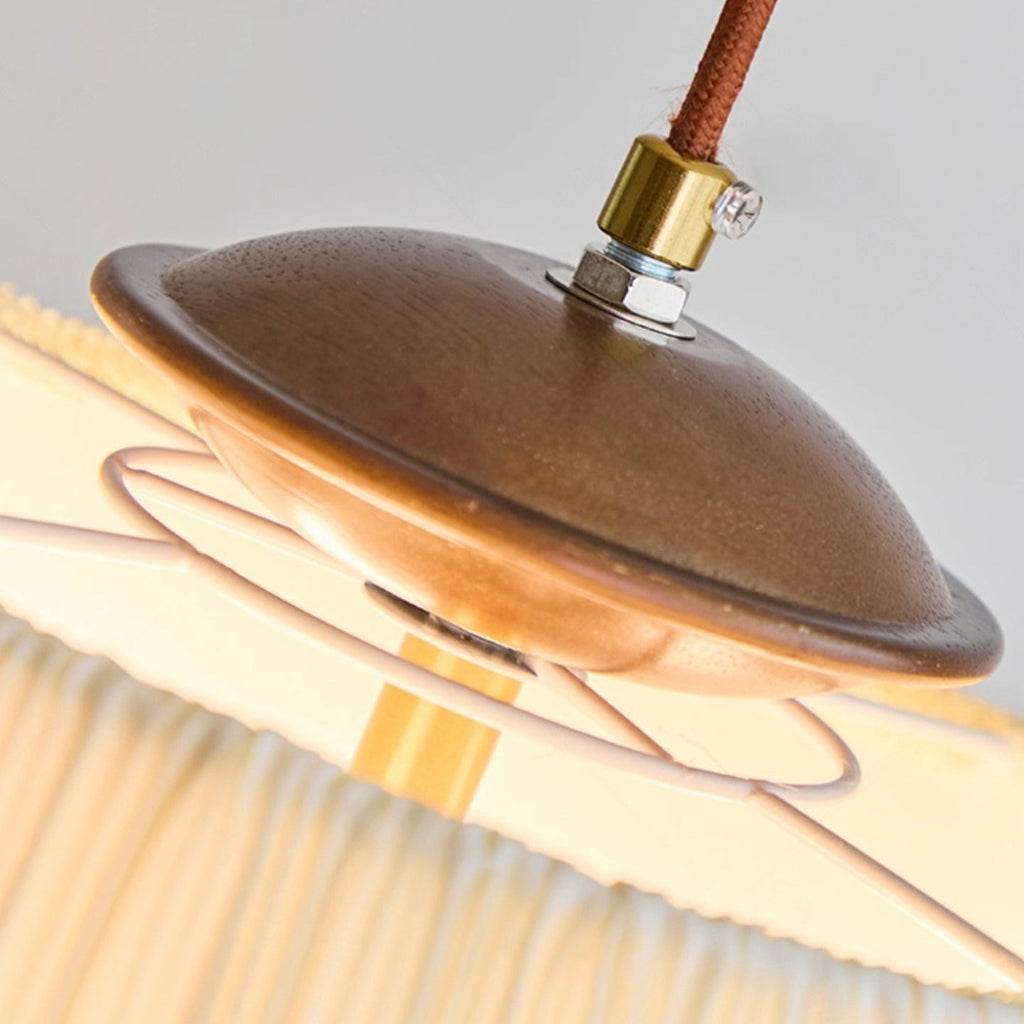 Close view of the walnut-toned canopy, brass cord grip and brown braided cord at the top of this Clérachic pendant.