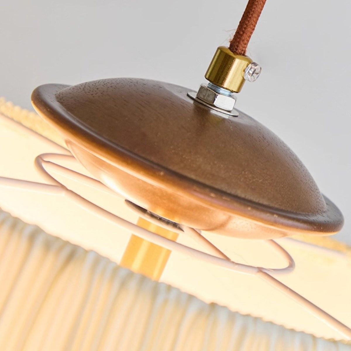 Close view of the walnut-toned canopy, brass cord grip and brown braided cord at the top of this Clérachic pendant.