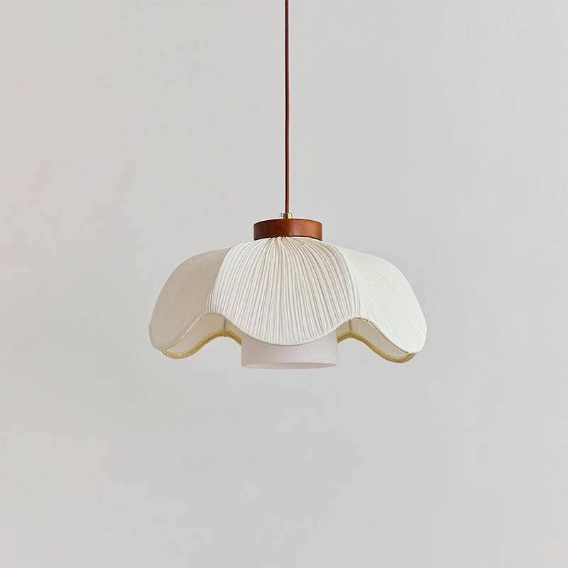 Side view of a Clérachic pendant with a wide, scalloped white pleated shade, a small walnut collar and an inner cylinder, on a light grey wall.