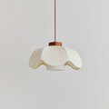 Side view of a Clérachic pendant with a wide, scalloped white pleated shade, a small walnut collar and an inner cylinder, on a light grey wall.