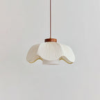 Side view of a Clérachic pendant with a wide, scalloped white pleated shade, a small walnut collar and an inner cylinder, on a light grey wall.