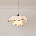 Lit two-tier pleated shade with dark-brown piped edges on a Clérachic pendant, hanging against a pale wall under white moulding.