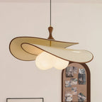 Beige version of this Clérachic pendant with a thin brown edge, its three opal globes lit, hanging in front of an arched pinboard.