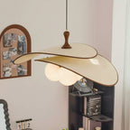 Beige shades of this Clérachic pendant seen from slightly below, hung near a black shelf with books, a record display and a sheer curtain.