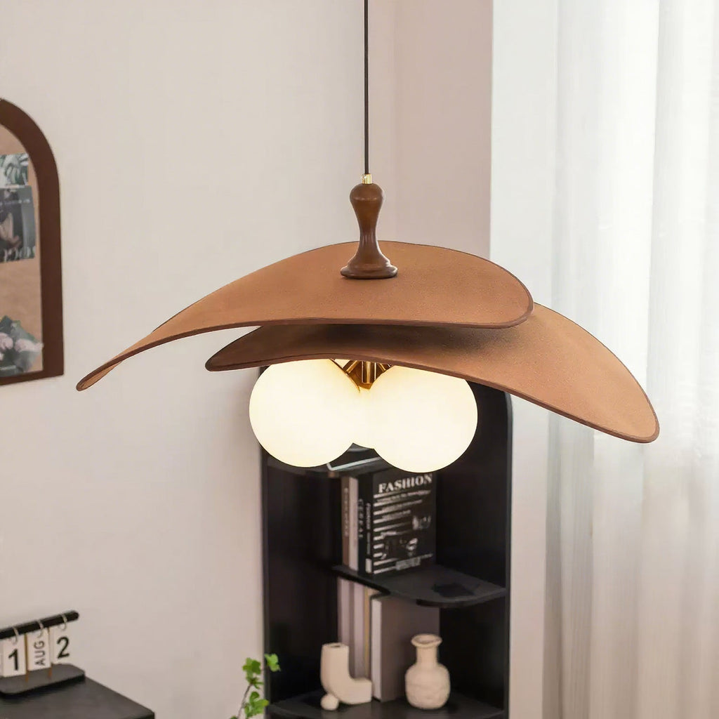 This Clérachic pendant in brown hangs above a black shelving unit with books and a small vase, with a sheer curtain at the window.