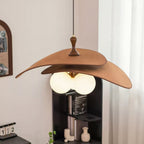 This Clérachic pendant in brown hangs above a black shelving unit with books and a small vase, with a sheer curtain at the window.