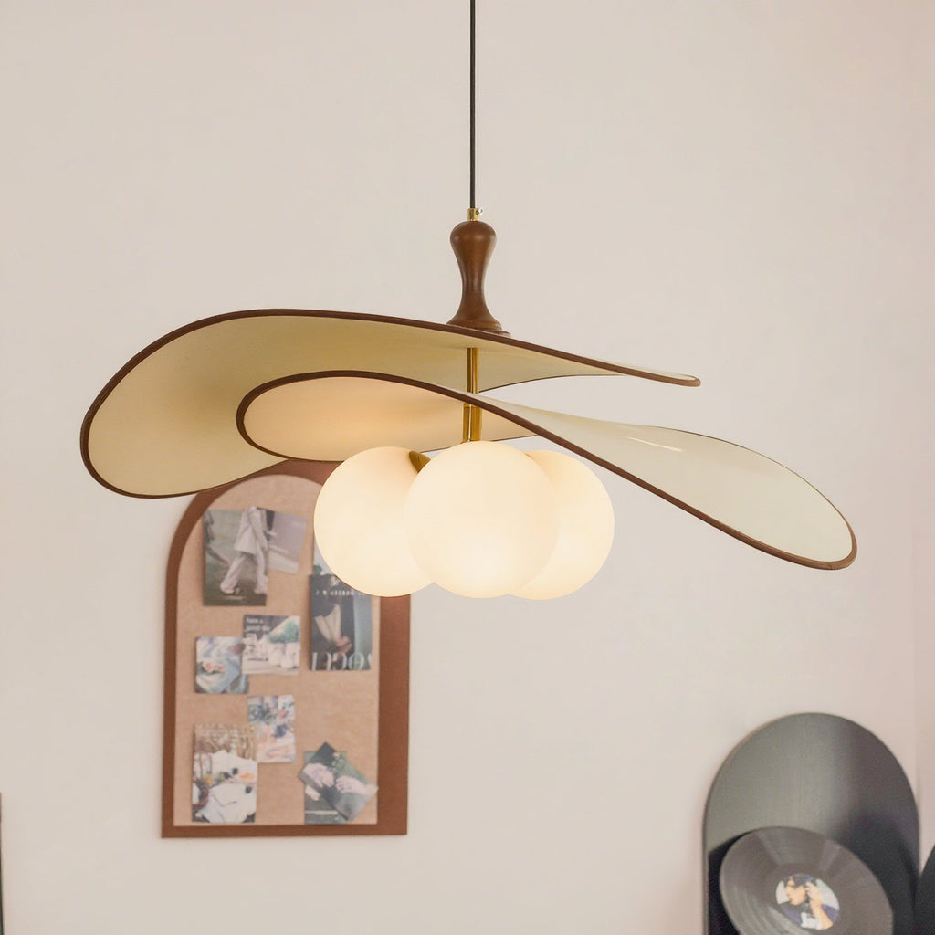 Wide view of the beige Clérachic pendant, with its turned wood stem and cluster of opal globes, beside an arched cork pinboard.