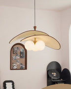 The beige Clérachic pendant hangs in a corner of a pale room, near an arched pinboard, a wavy mirror frame and a black display shelf.
