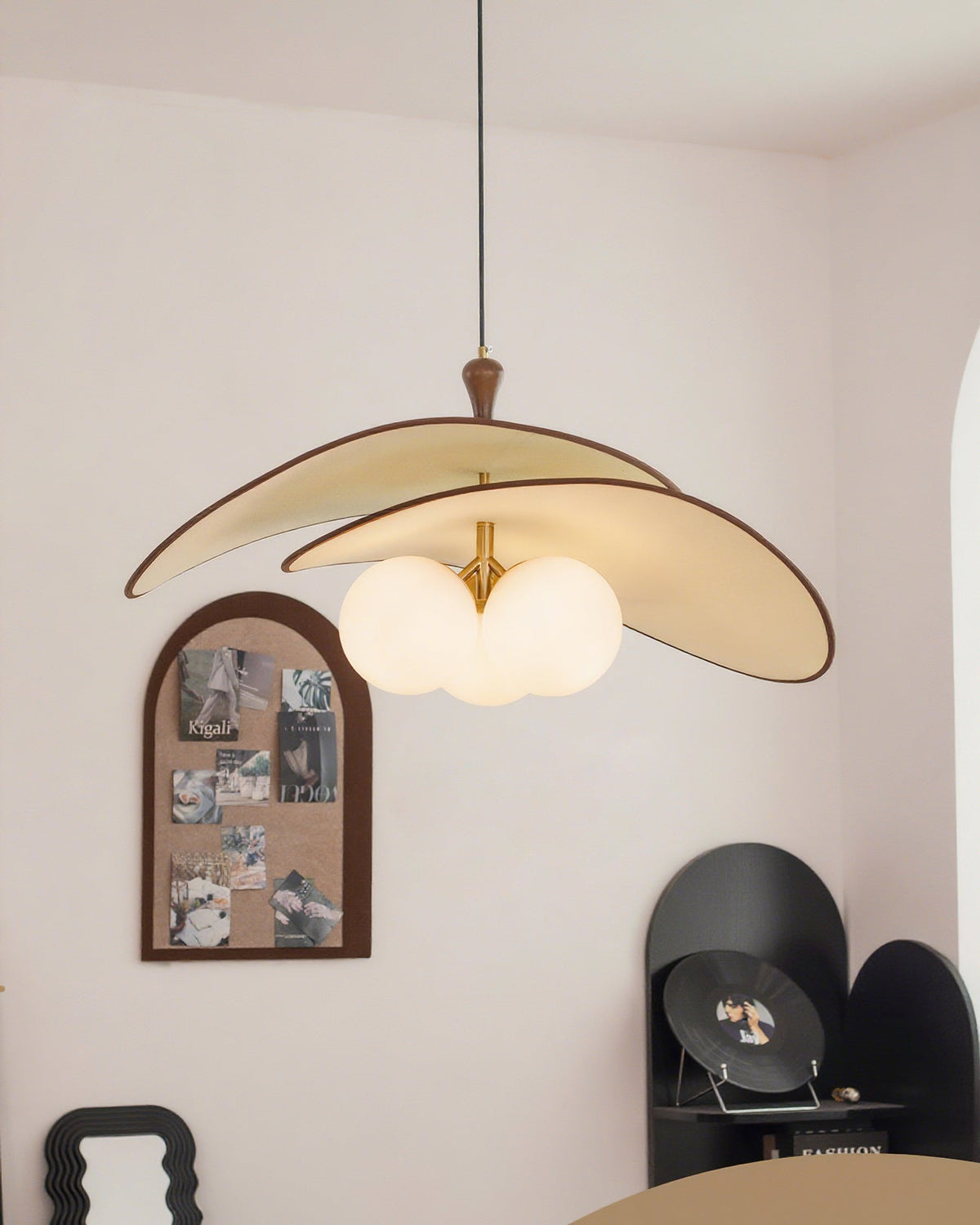 The beige Clérachic pendant hangs in a corner of a pale room, near an arched pinboard, a wavy mirror frame and a black display shelf.