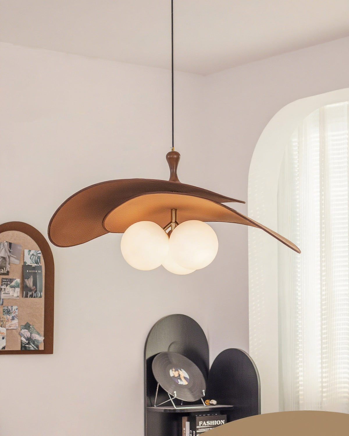 Brown Clérachic pendant seen from further back, hung near an arched pinboard and a curtained window with a black shelf below.
