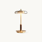 Clérachic table lamp on a plain white backdrop, a clear glass dish shade over a slim brass stem, walnut section and round brass base.