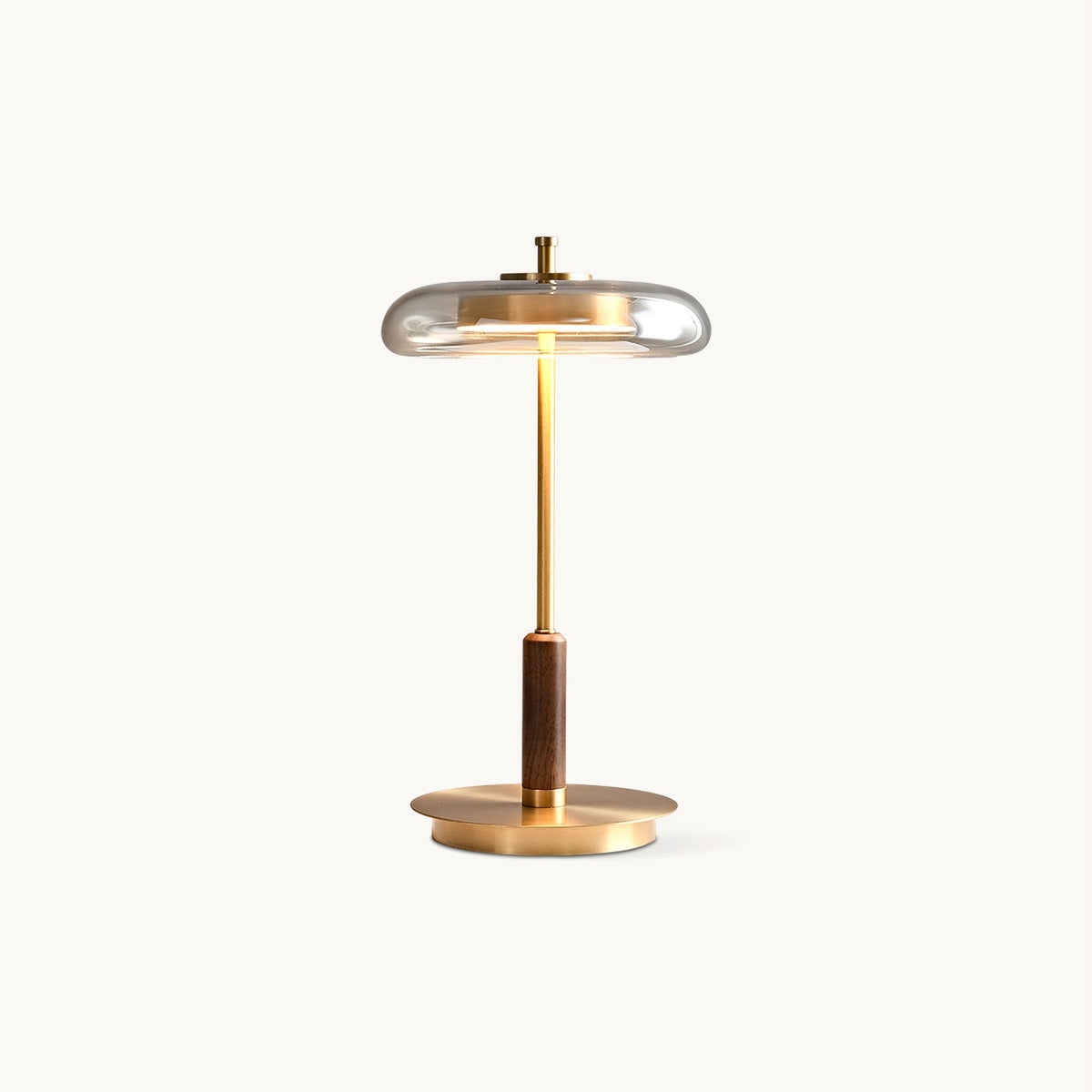 Clérachic table lamp on a plain white backdrop, a clear glass dish shade over a slim brass stem, walnut section and round brass base.