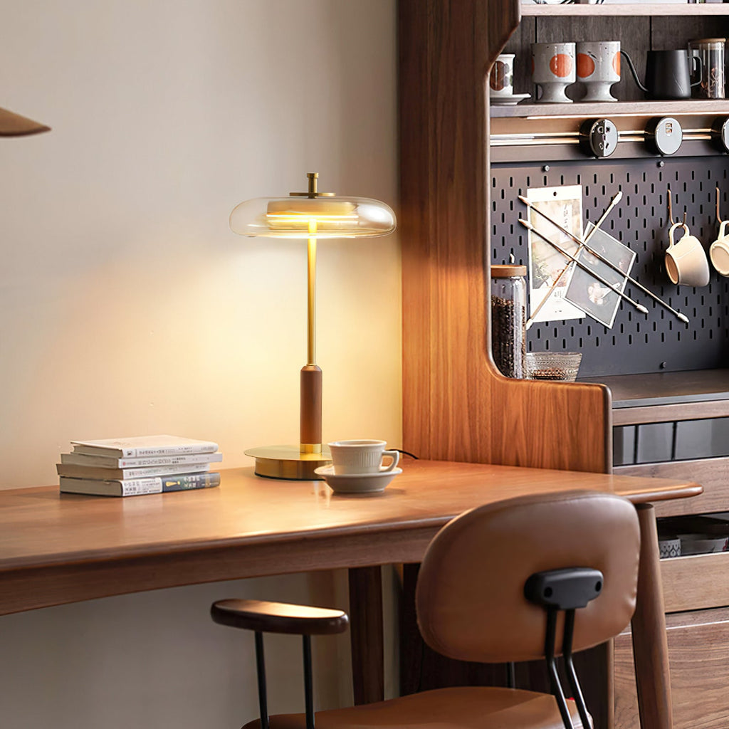 Walnut desk corner with a Clérachic table lamp switched on, books and a cup at its base and a pegboard shelf behind.