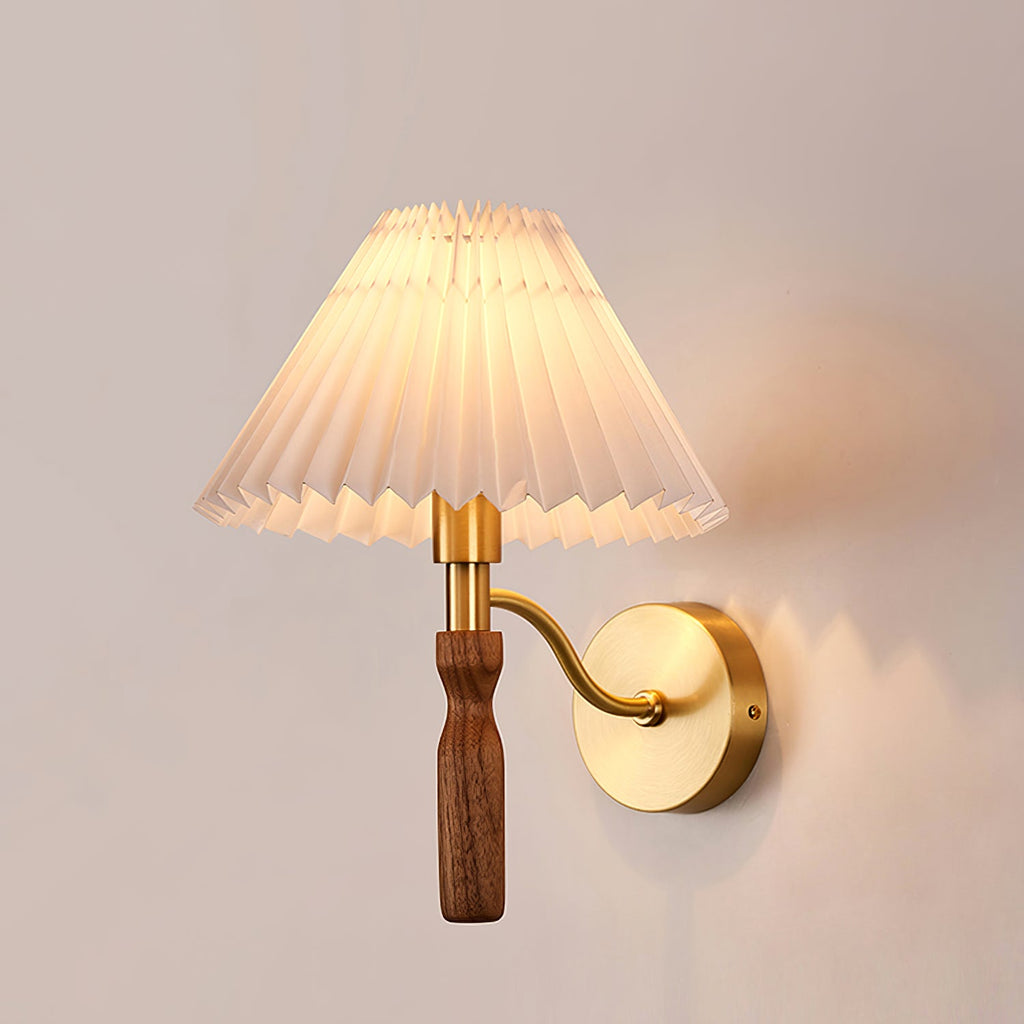 Side view of a lit Clérachic wall light, its curved brass arm holding a walnut grip and a pleated shade against a soft pink wall.