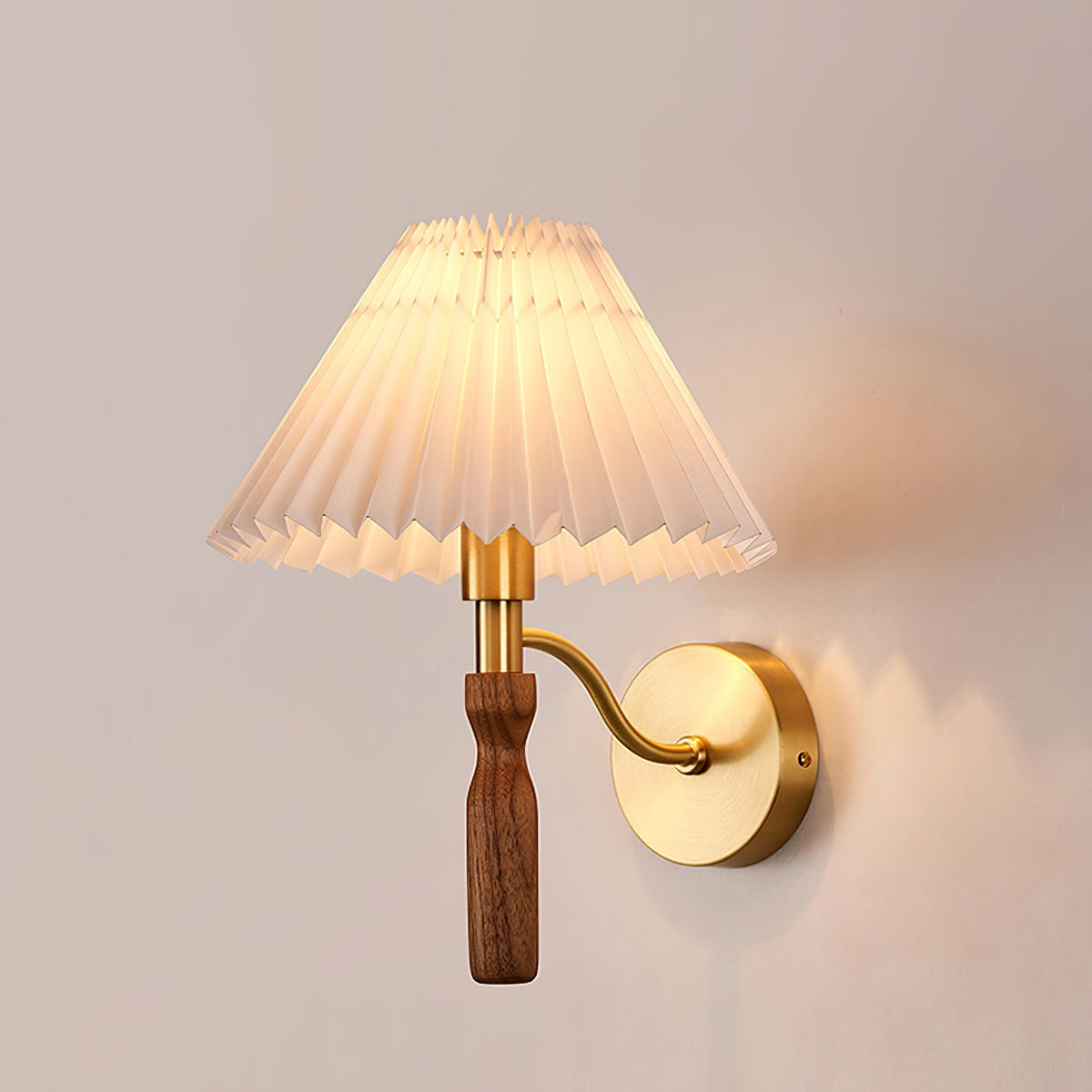 Side view of a lit Clérachic wall light, its curved brass arm holding a walnut grip and a pleated shade against a soft pink wall.