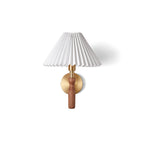 Clérachic wall light on a white backdrop with a soft shadow, a pleated shade over a short walnut stem and brass plate.