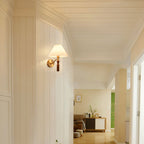 A Clérachic wall light lit in a white-panelled hallway, with a bright living room visible further along.