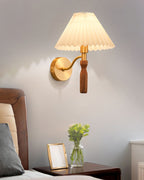 Clérachic wall light on a grey wall above a wood bedside table, with a framed photo, a glass vase of green stems and a wooden bed head.