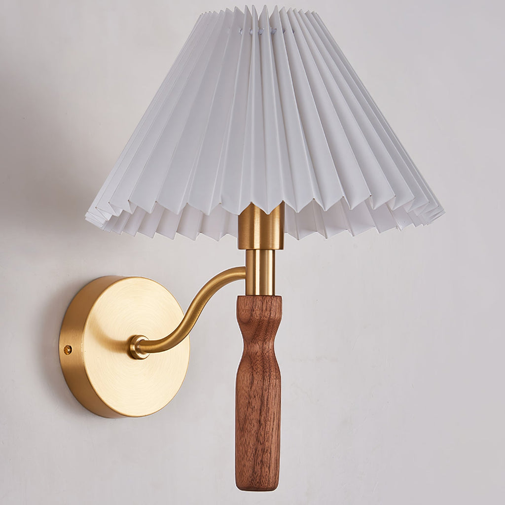 Close view of the pleated shade, brass fitting and walnut grip of this Clérachic wall light on a pale wall.