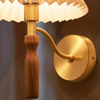 Close view of the brass back plate, curved arm and walnut grip of this Clérachic wall light, lit against a warm brown wall.
