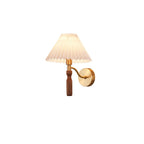 Small Clérachic wall light on a white backdrop, with a pleated shade and a curved brass arm to a walnut grip.