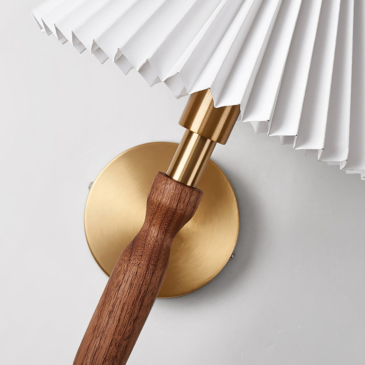 Close view of the brass collar, walnut grip and pleated shade edge of this Clérachic wall light, against a pale wall.
