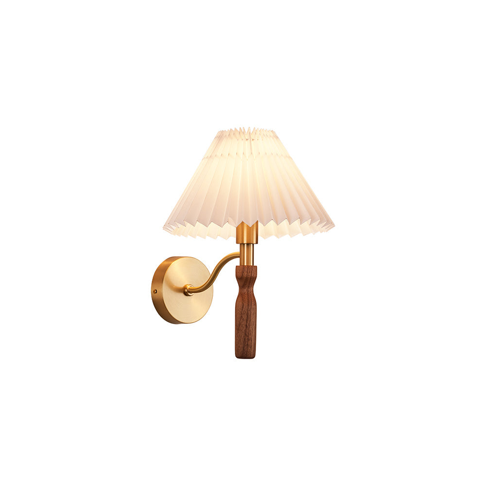 This Clérachic wall light on a white backdrop, lit softly, with a pleated shade, S-curved brass arm and walnut handle.