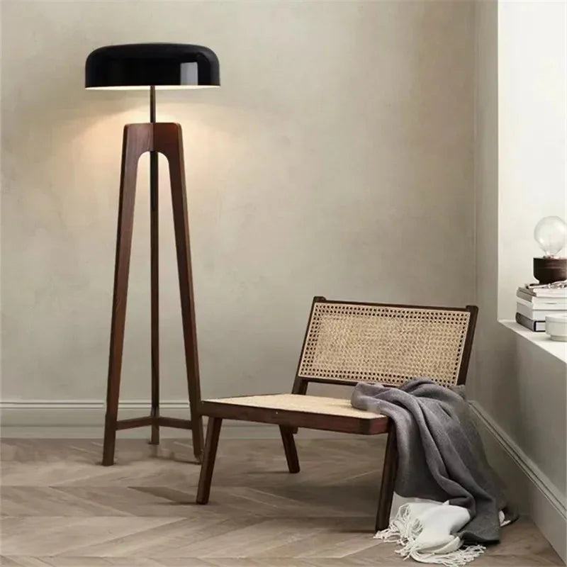 Clérachic wood tripod floor lamp lit beside a cane-backed bench, its splayed legs standing on herringbone parquet.
