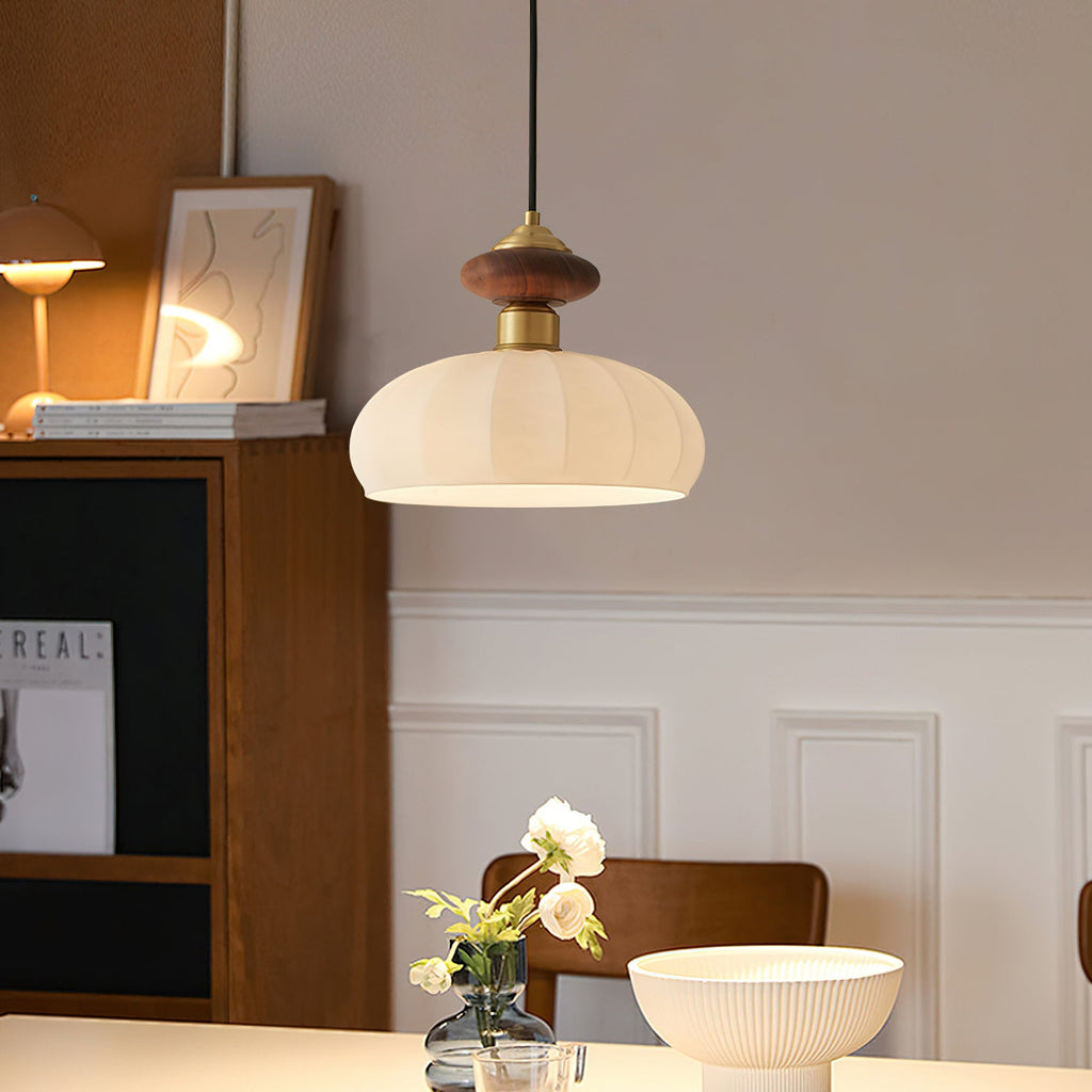 This Clérachic pendant glows over a dining table, with a walnut and brass top, a ribbed glass shade and a white-panelled wall behind.