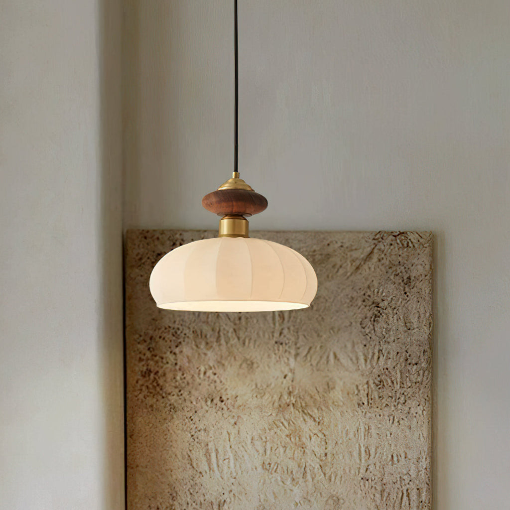 A Clérachic pendant with a lit ribbed glass shade hangs in front of a textured beige canvas on a pale wall.