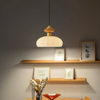 Lit Clérachic pendant over a dining table, with a warm wooden knob, a ribbed shade and picture shelves on a grey wall.
