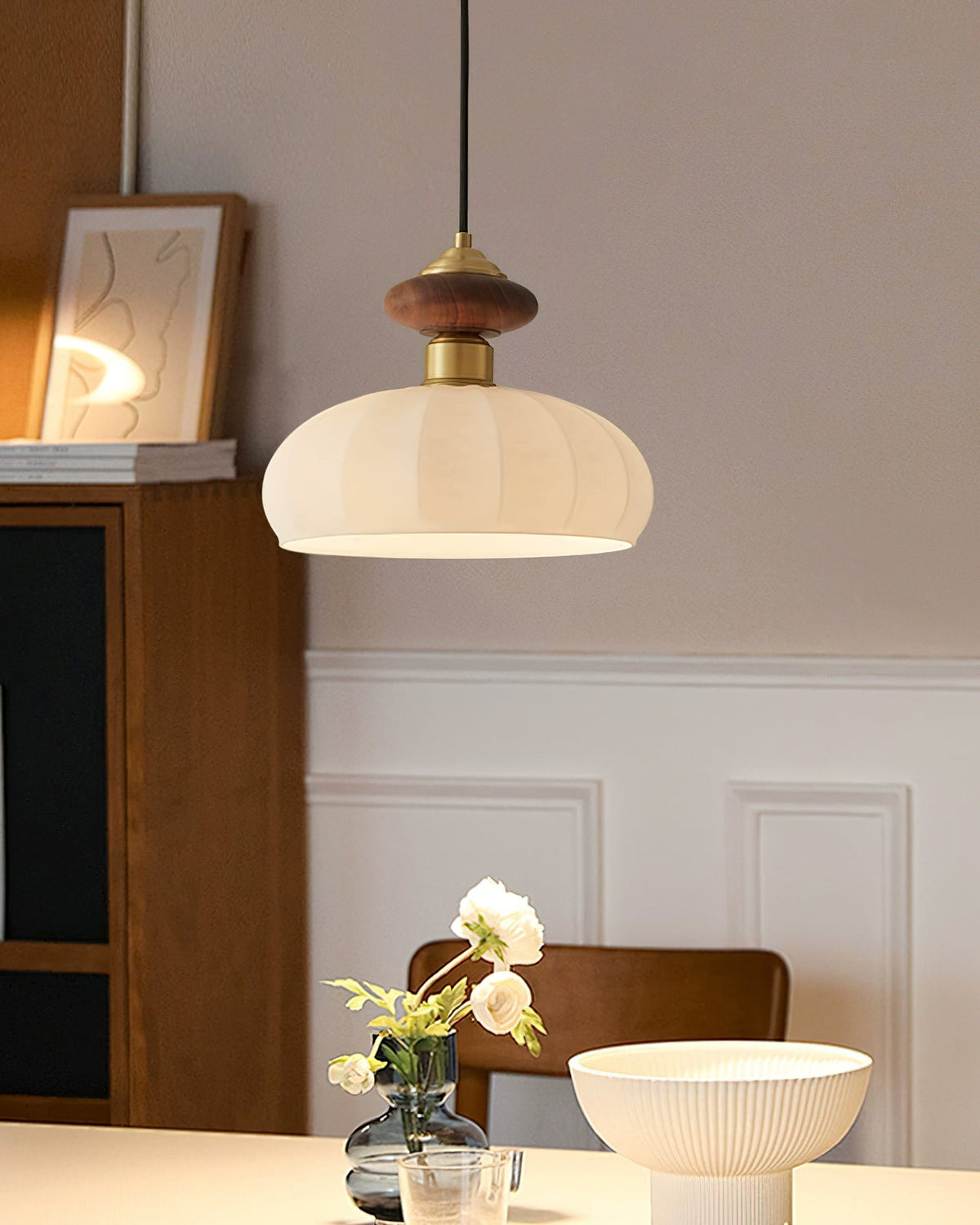 A Clérachic pendant with a ribbed glass shade hangs near a framed print and a wooden cabinet above a bowl and flowers.