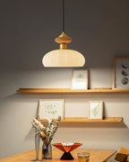 This Clérachic pendant casts a pool of light on a grey wall with two shelves of small framed prints and a vase of dried stems.