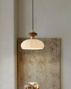 Narrow view of a Clérachic pendant with walnut and brass top, hung in front of a large textured canvas on a plain wall.