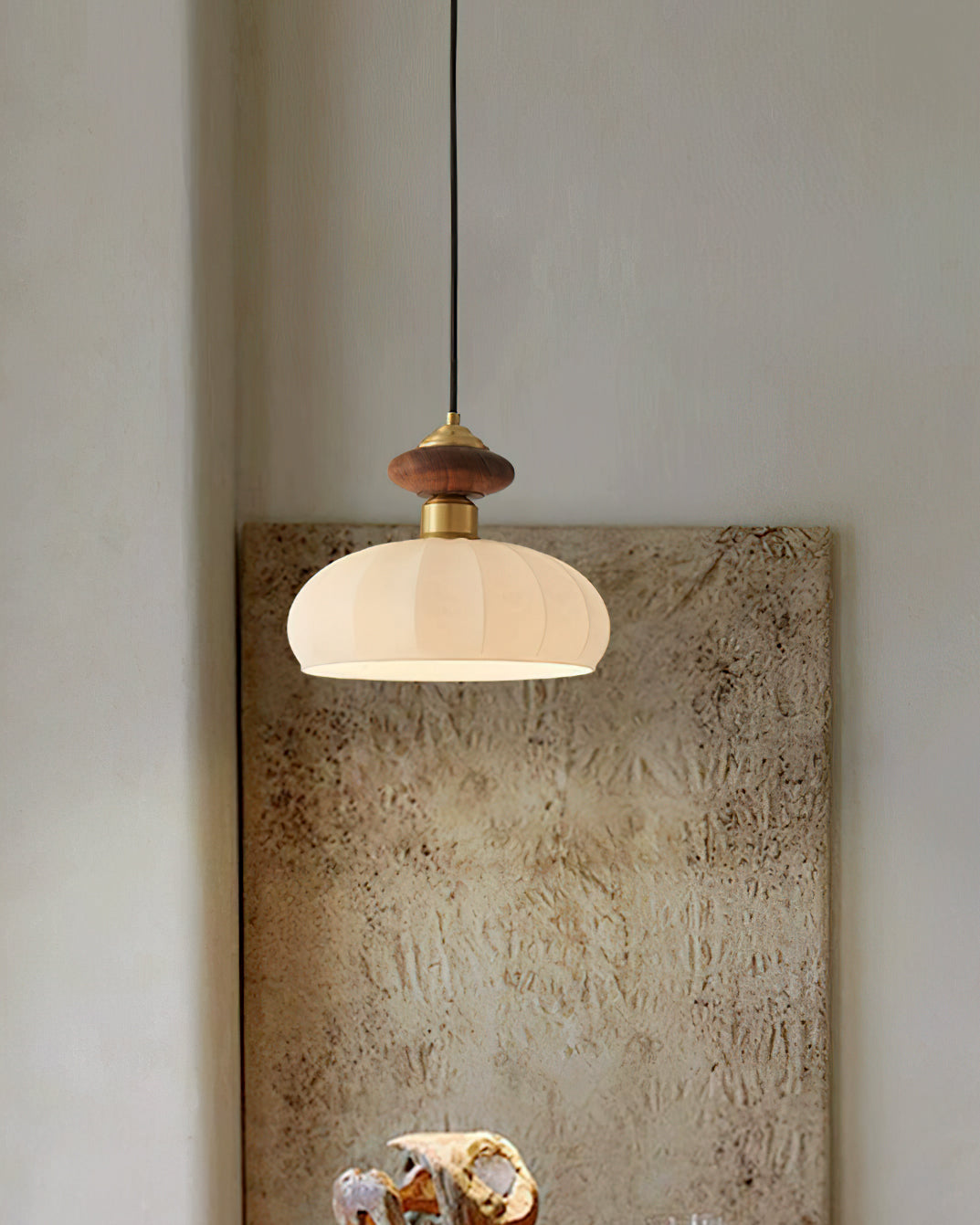 Narrow view of a Clérachic pendant with walnut and brass top, hung in front of a large textured canvas on a plain wall.