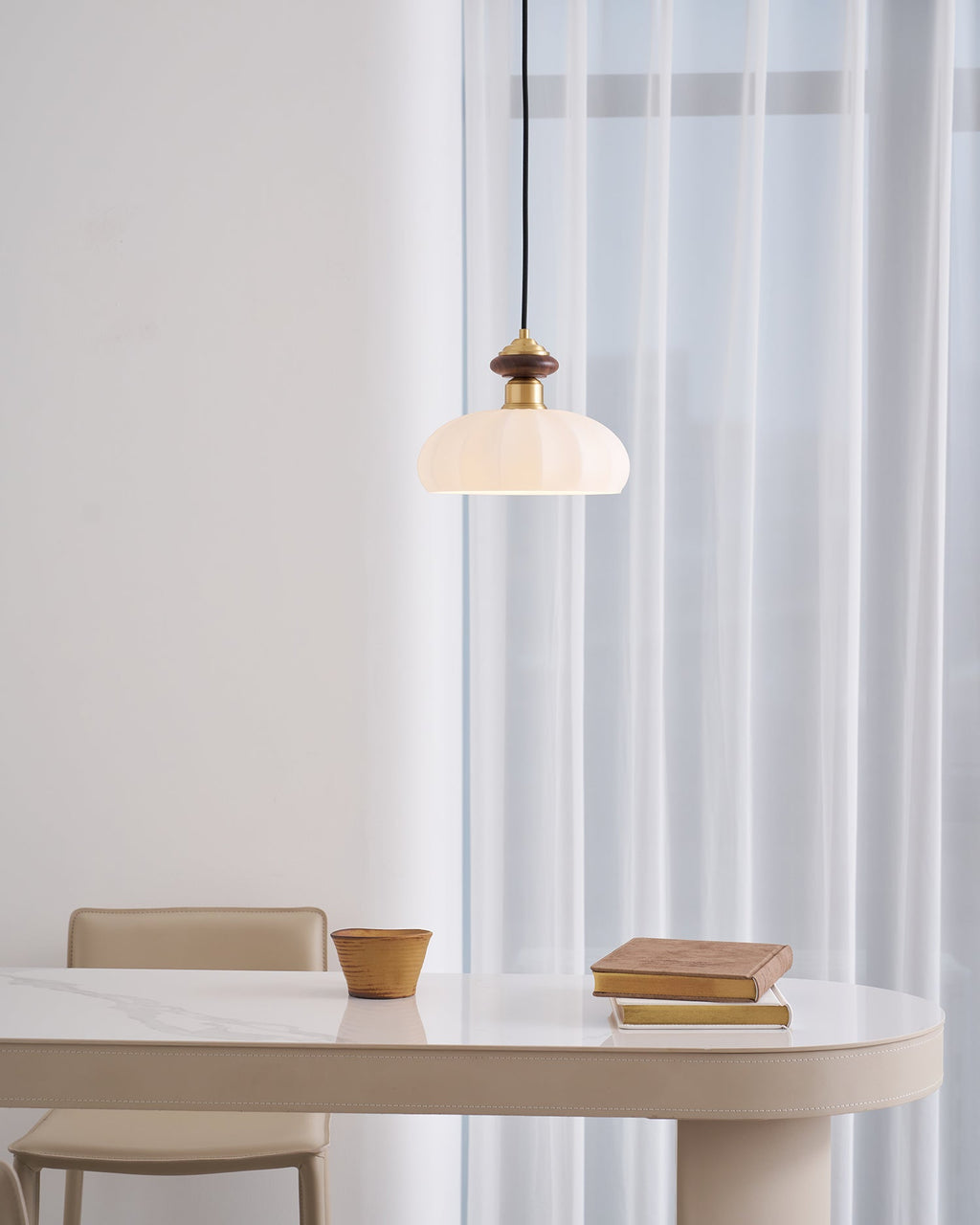 This Clérachic pendant glows in a bright, airy room, hung above a curved table with a clay pot and books near sheer curtains.