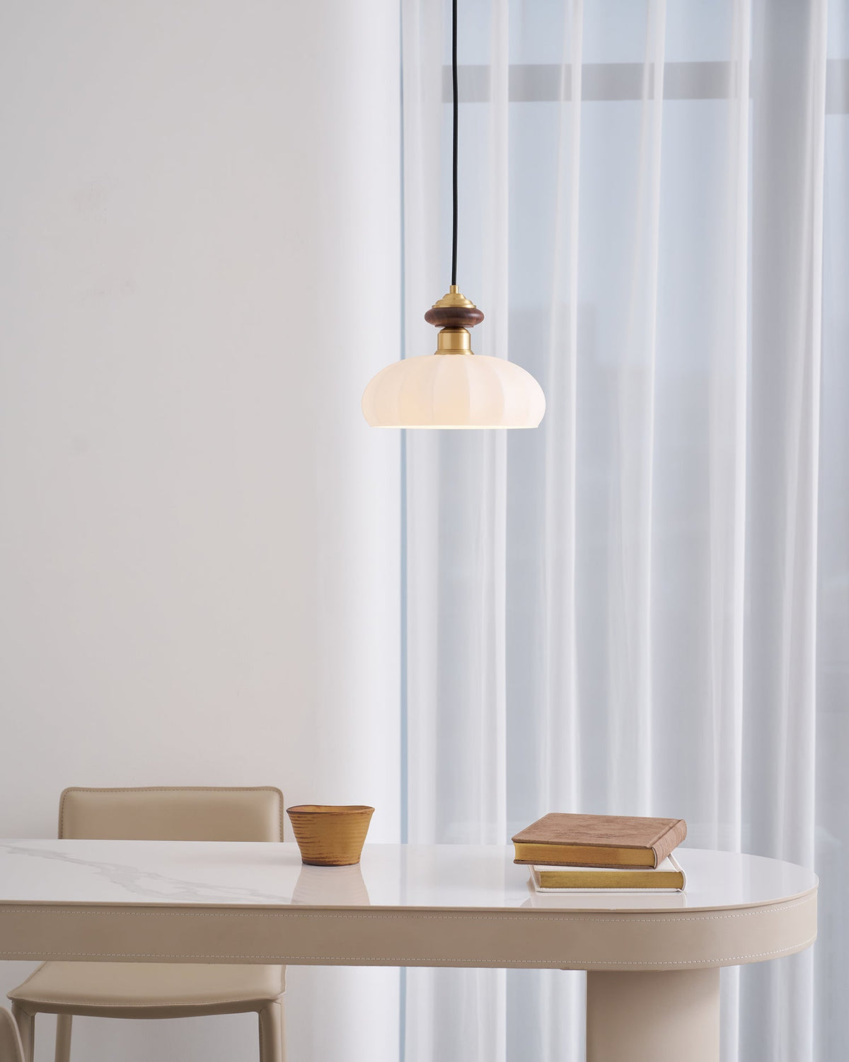 This Clérachic pendant glows in a bright, airy room, hung above a curved table with a clay pot and books near sheer curtains.