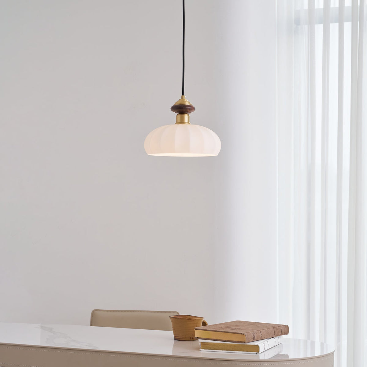 A Clérachic pendant with a ribbed glass shade and walnut and brass top hangs near a curtain, with a marble table below.