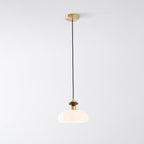 A Clérachic pendant with a warmly lit ribbed shade, walnut-coloured knob and brass canopy, on a pale grey backdrop.