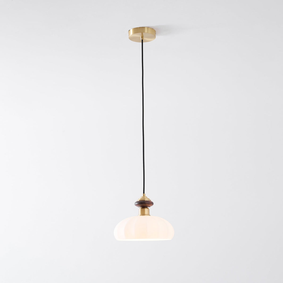 A Clérachic pendant with a warmly lit ribbed shade, walnut-coloured knob and brass canopy, on a pale grey backdrop.