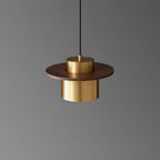Brass cylinder shade under a round walnut brim on this Clérachic pendant, shown against a mid-grey backdrop.