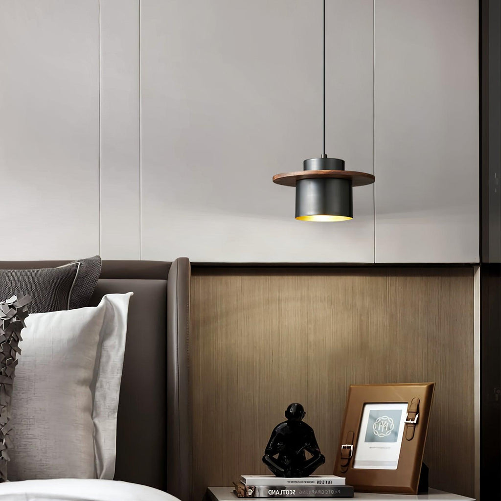Black-and-walnut Clérachic pendant hangs above a bedside table with a framed picture and a sculpture, in front of a dark panel headboard.