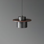 Front view of a black-and-walnut Clérachic pendant, its dark metal cylinder under a round walnut brim, on a grey backdrop.