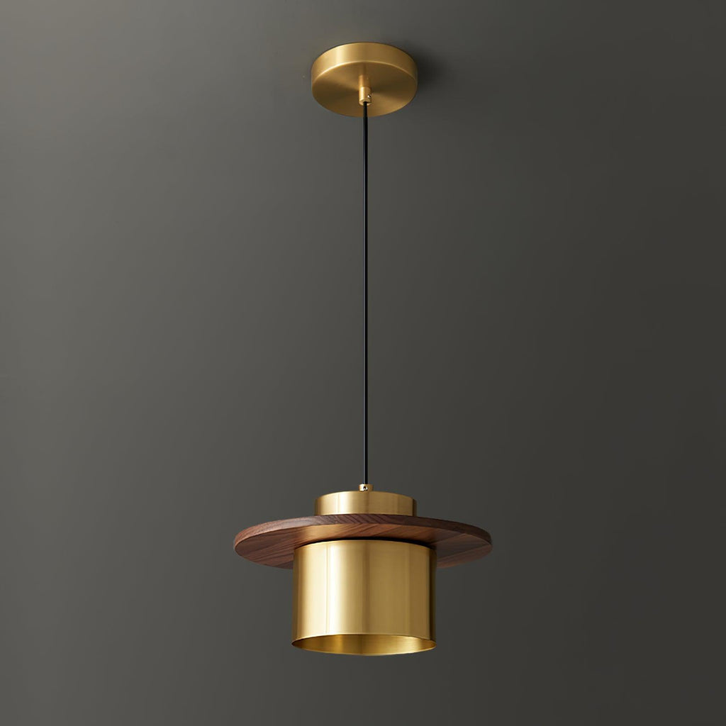 A Clérachic pendant with a round brass canopy, black cord and walnut-brimmed brass shade, shown against a dark grey wall.