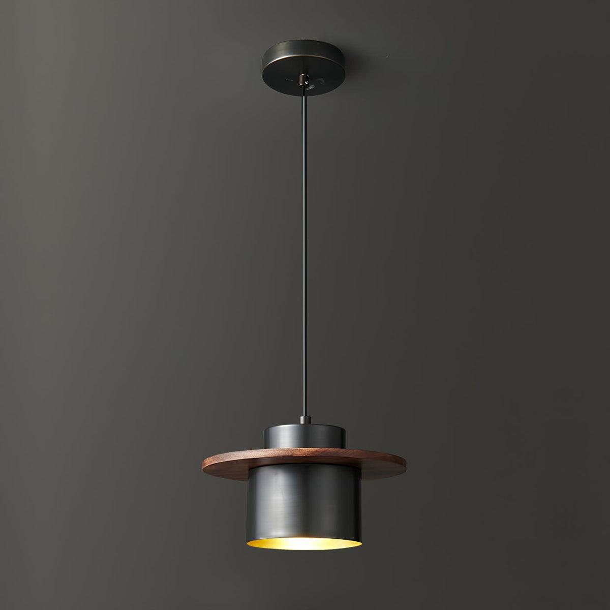 A Clérachic pendant with a black canopy and cord and a dark cylinder shade under a walnut brim, shown against charcoal.