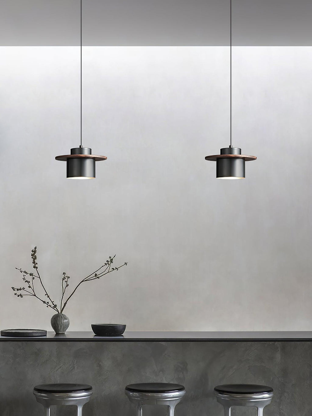Two small black-and-walnut Clérachic pendants hang above a grey concrete-look counter with three dark stools.
